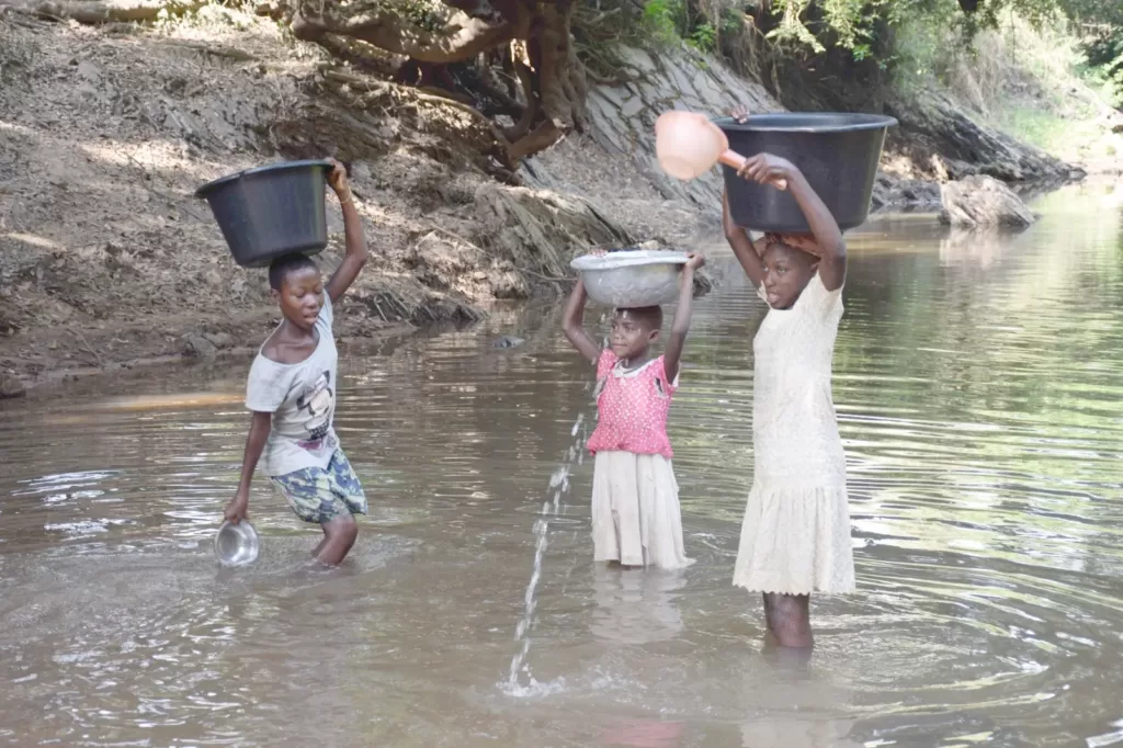 Girls Filling Their Buckets To The Top With Stream Water